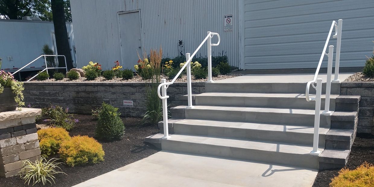 A concrete staircase with aluminum railings on both sides leads up to a white door.
