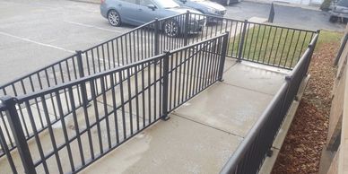 An outdoor setting with a black aluminum railing installed alongside a concrete ramp