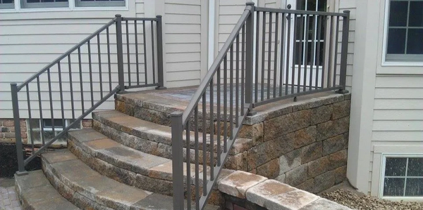 The steps have bronze aluminum railings on both sides and are flanked by matching stone walls.