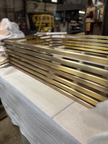 Shiny brass watchbands stacked on fabric surface in a workshop.