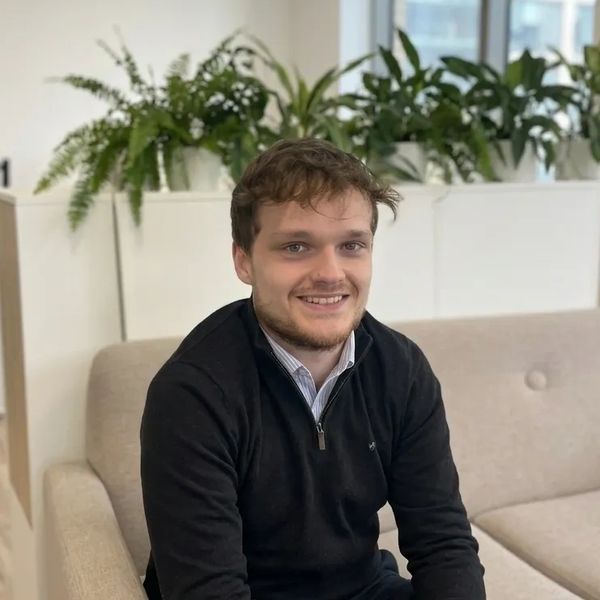 A young man sitting on a beige couch smiling at the camera.