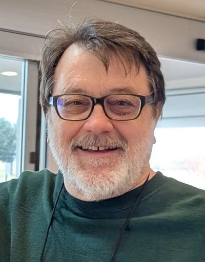 Photo of Guy's happy smiling face with dark glasses, brown hair, and a light gray beard