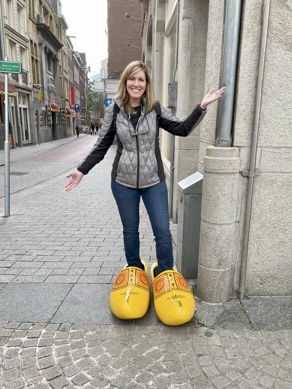 Woman posing in oversized yellow clogs on a cobblestone street in Amsterdam.