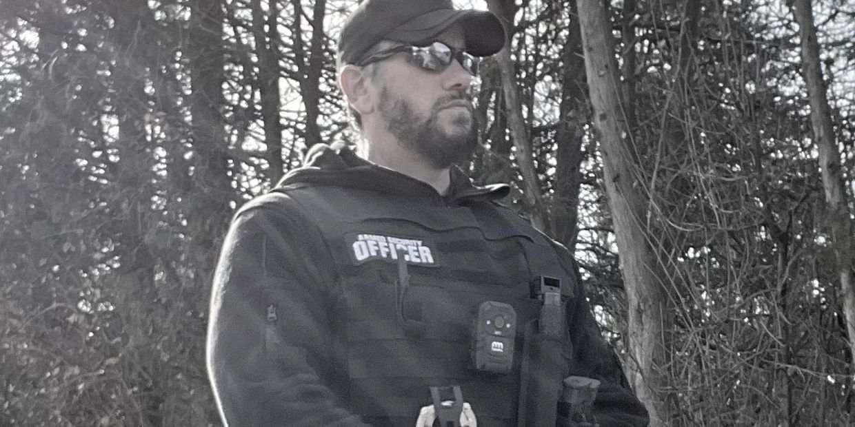 Man in tactical gear labeled 'Officer' outdoors.