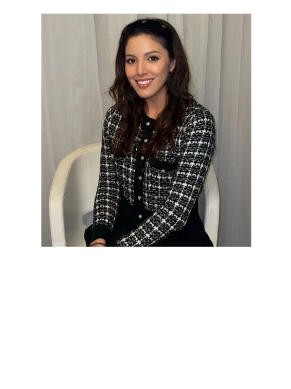 A smiling woman with long hair sits on a white chair against a light curtain background.