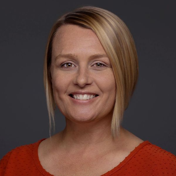 Smiling woman with short blonde hair and red top against dark background.
