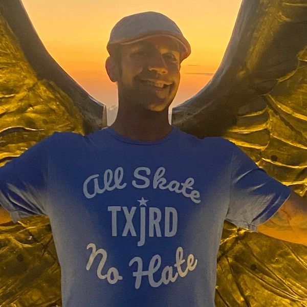 Man smiling with golden wings and sunset background.