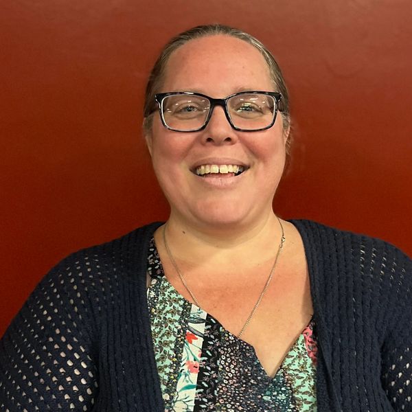 Smiling woman with glasses in front of a red background.
