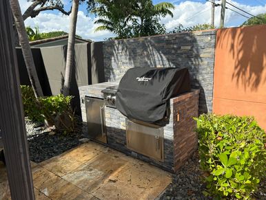 Outdoor kitchen with a covered grill and stone wall.