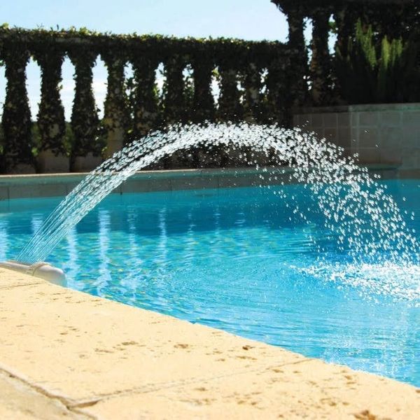 Water fountain spraying a clear arc into a bright blue swimming pool.