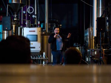 A speaker presenting in an industrial setting with an audience.