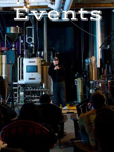 A speaker presents at an event in an industrial-style venue with brewing equipment.
