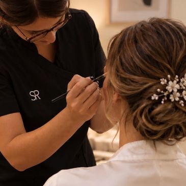 Maquilladora aplicando maquillaje a una novia con recogido elegante.