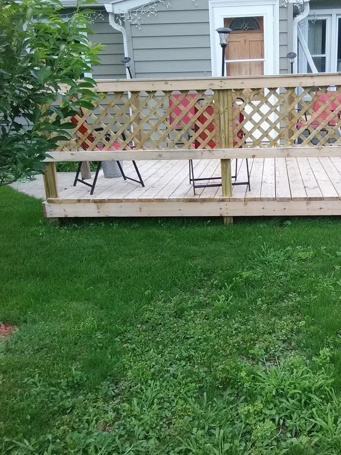 A small wooden deck with lattice railing and red chairs in a backyard.