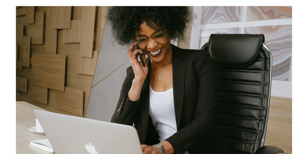 A woman sitting at her her desk in front of her computer, laughing on the phone