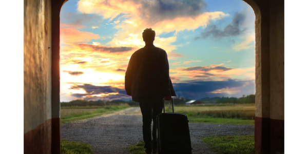 A man with a suitcase viewing the sunset as he walks through a doorway 