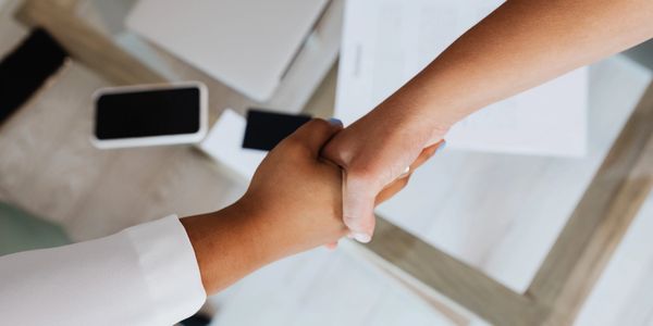 Two arms reaching to shake hands across a desk 