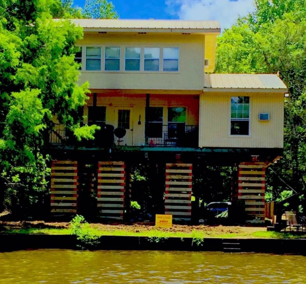 A stilt house elevated above the ground near a water body surrounded by greenery.