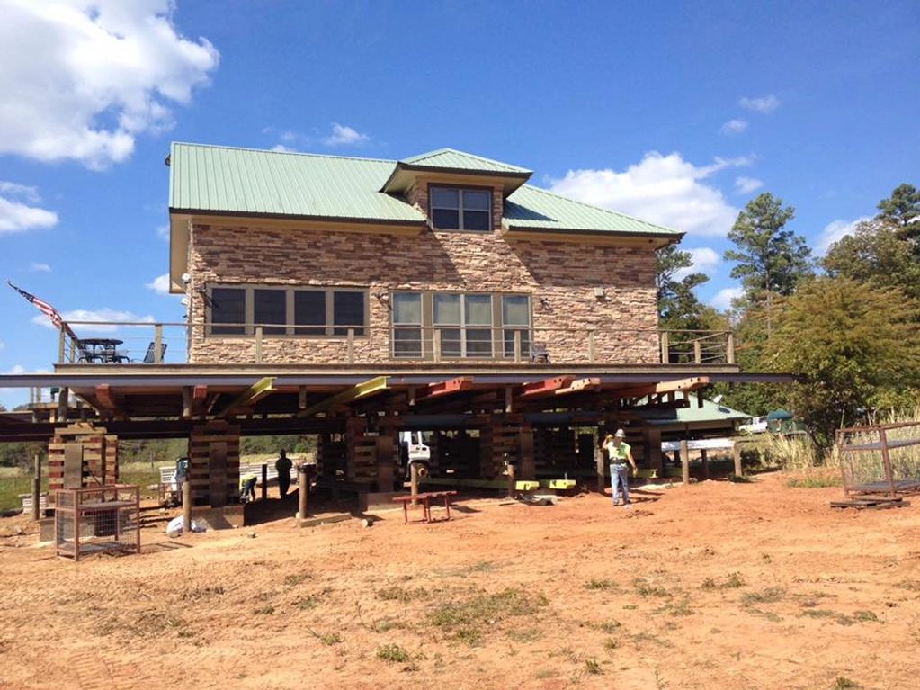 House elevated on jacks for foundation work under a clear blue sky.