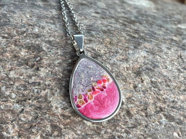 Teardrop-shaped pendant with pink and purple resin on a silver chain.