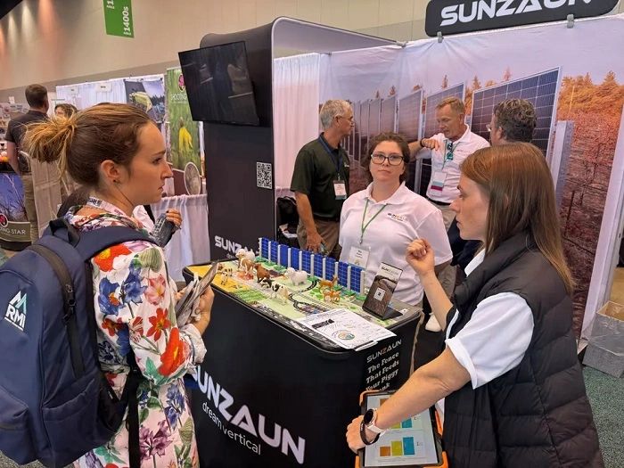 People discuss solar panel model at expo booth.