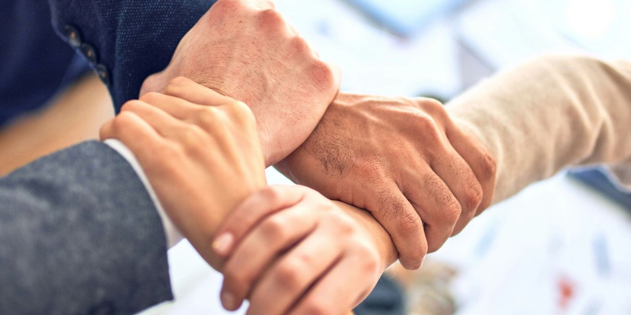 Four hands gripping each other's wrists in a team unity gesture.
