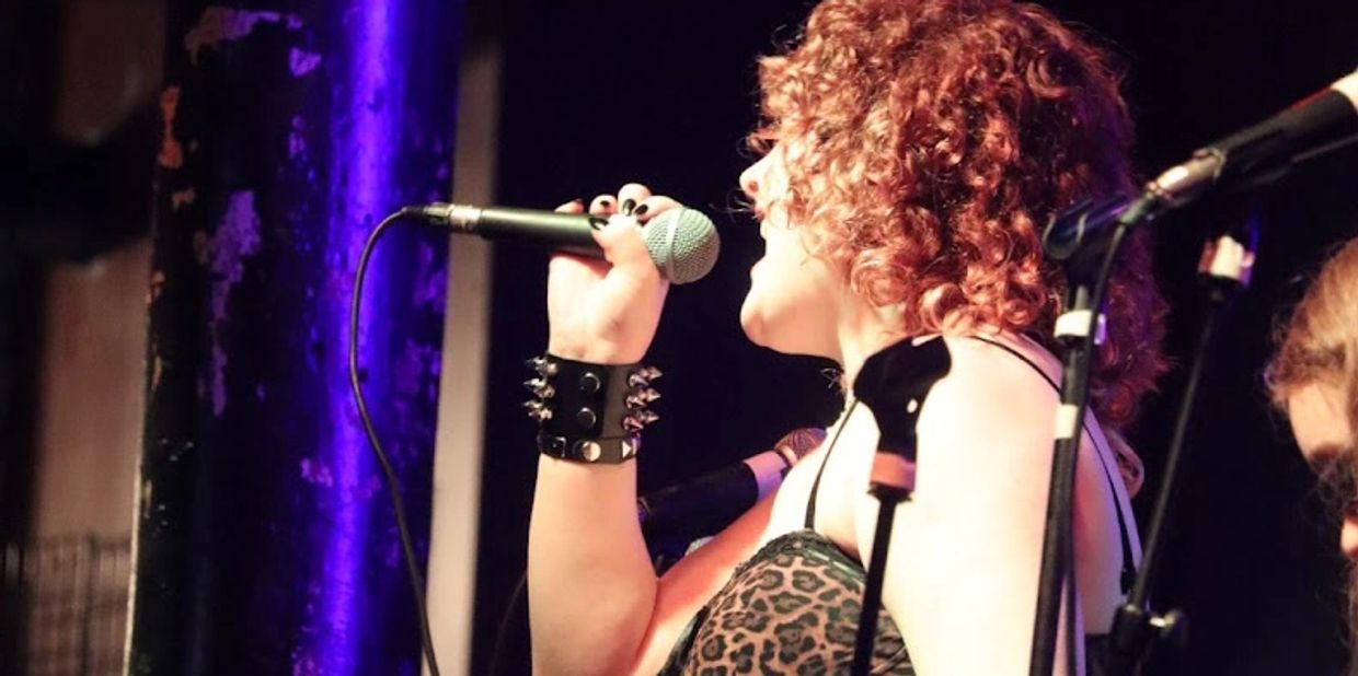 Curly-haired singer passionately performs on stage with a microphone.
