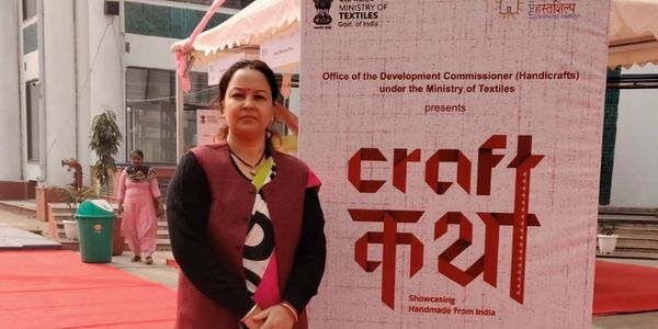 Woman standing next to a banner for a handmade crafts event in India.
