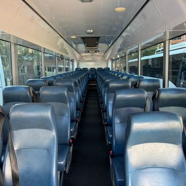 Empty bus interior with rows of blue leather seats and large windows.