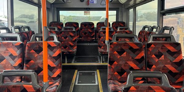 Empty bus interior with patterned red and black seats and orange poles.