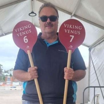 Man holding Viking Venus paddles numbered 6 and 7 under a tent.