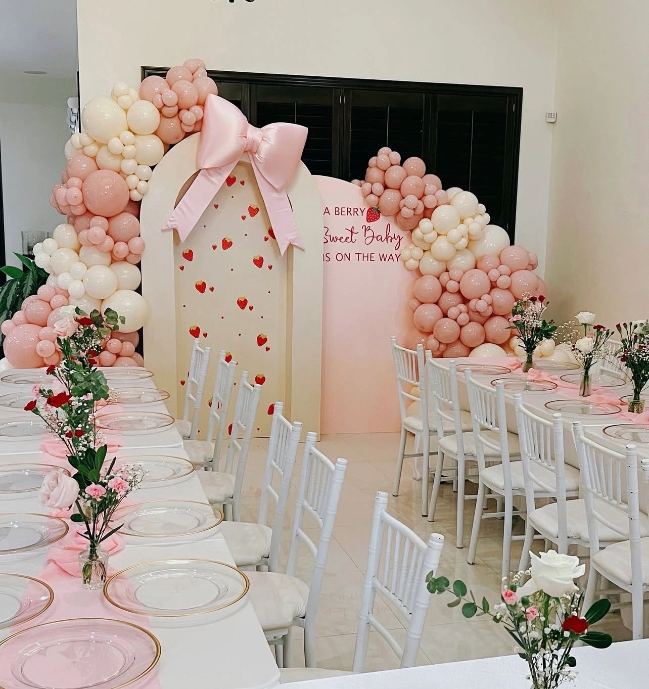 Elegant pink and white baby shower setup with balloon arch and floral table decor.