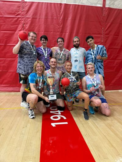 A winning dodgeball team posing with trophies indoors.