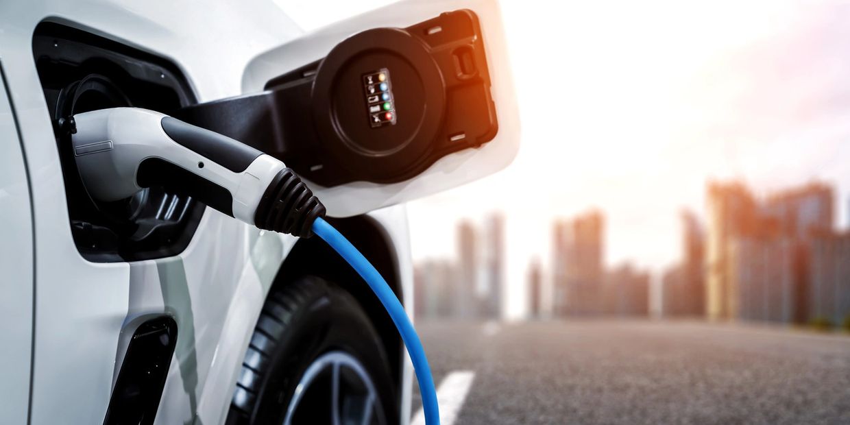 Close-up of an electric car charging with a blue cable in a city setting.