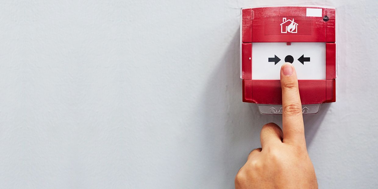 Finger pressing a red fire alarm on a wall.