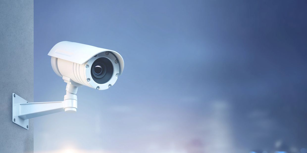 White security camera mounted on a wall against a blue background.