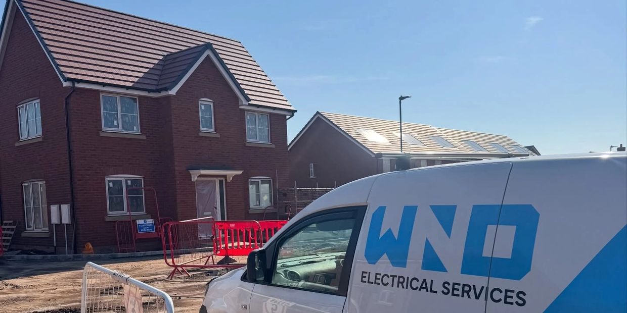 A white electrical services van near new brick houses under construction.