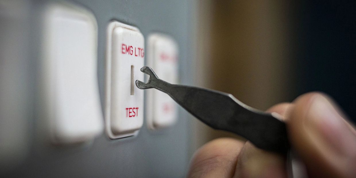 A person uses a tool to press an emergency light test switch.