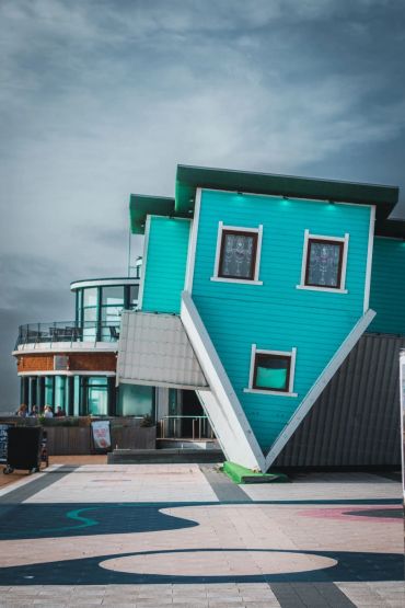 An upside-down turquoise house in an urban area.