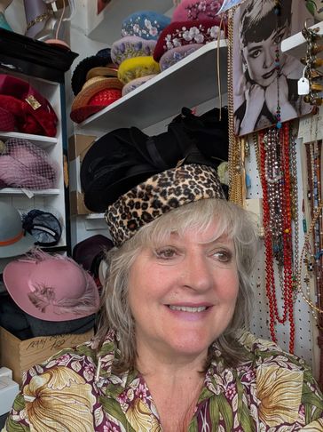 Smiling woman wearing a leopard print hat in a colorful hat shop.