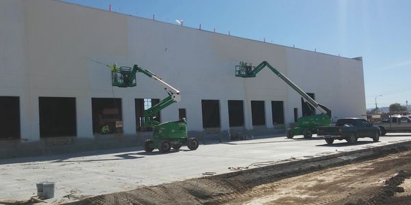 Two green boom lifts working on a building's exterior.