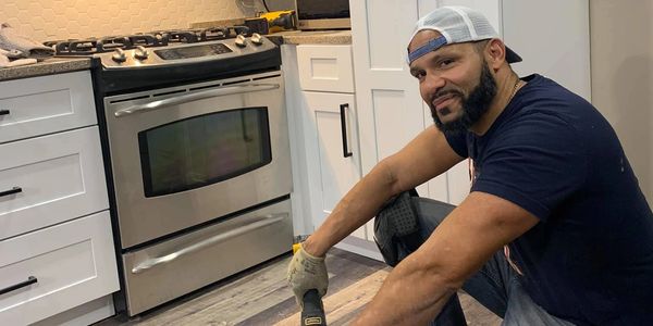 residential kitchen remodel in progress with a worker smiling while installing new flooring