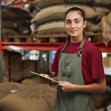 Mujer joven con bata revisando inventario en almacén.