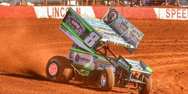 A sprint car racing on a dirt track, kicking up dust.