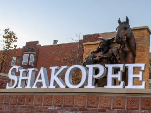 Statue of a Native American and horse with 'SHAKOPEE' sign in a town setting.