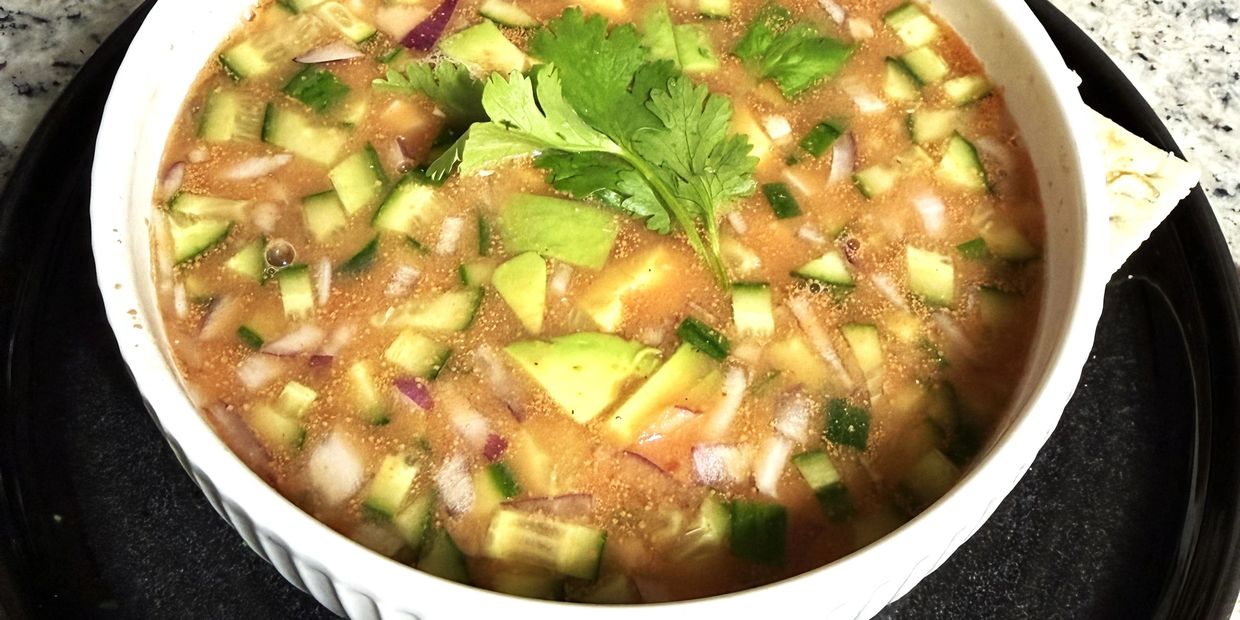 A bowl of fresh vegetable soup garnished with cilantro on a black plate.
