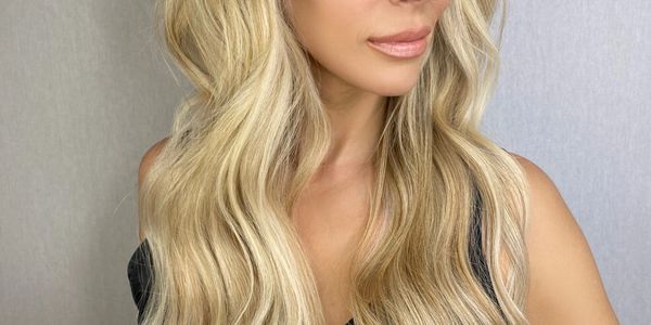 Blonde woman with long wavy hair looking sideways in a black top.