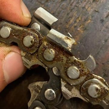 Close-up of a rusty chainsaw chain being held.