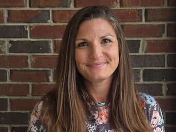 Woman smiling with long brown hair against a brick wall.