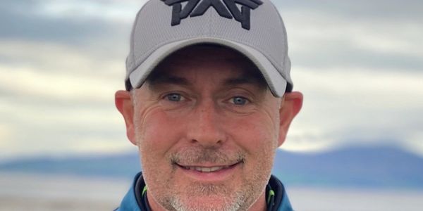 Man smiling outdoors wearing a gray cap and blue jacket.